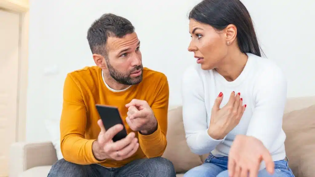 A man in yellow points at a phone while talking to a woman in white.