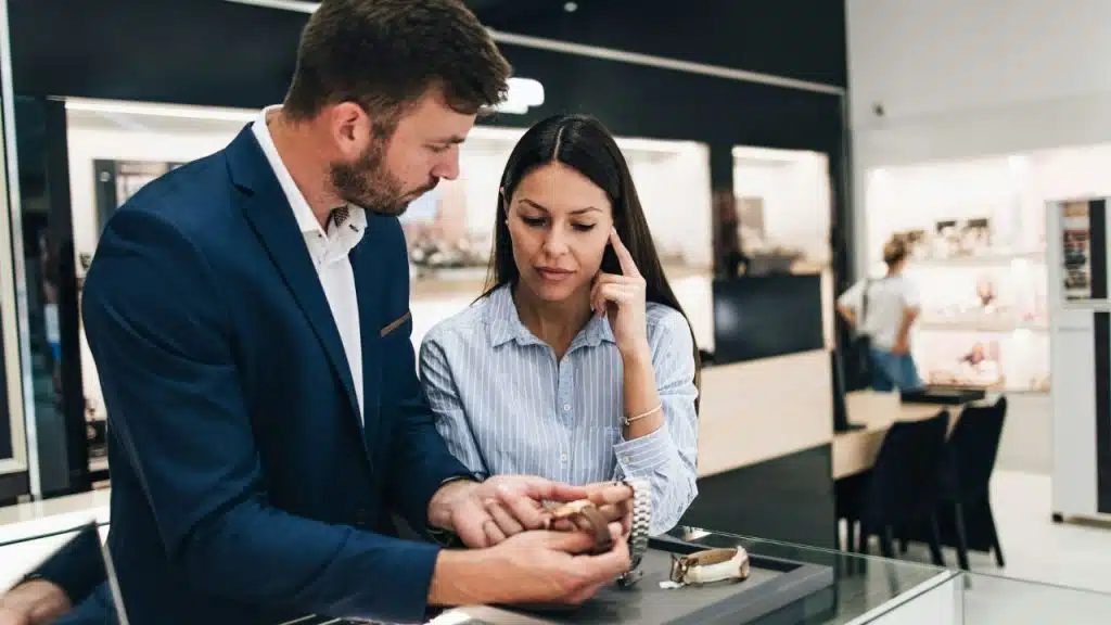 A man in a blue suit and a woman look at watches in a store.