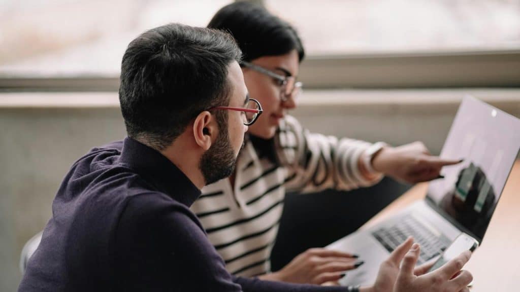 A man and woman working together on a laptop, with the woman pointing at the screen.