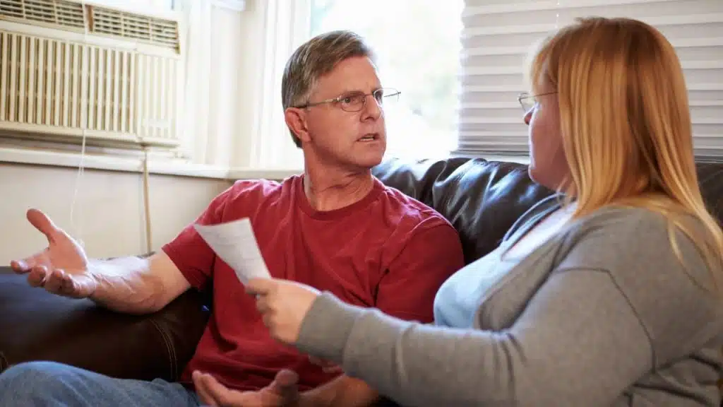 A man in a red shirt gestures while looking at a woman holding a paper.