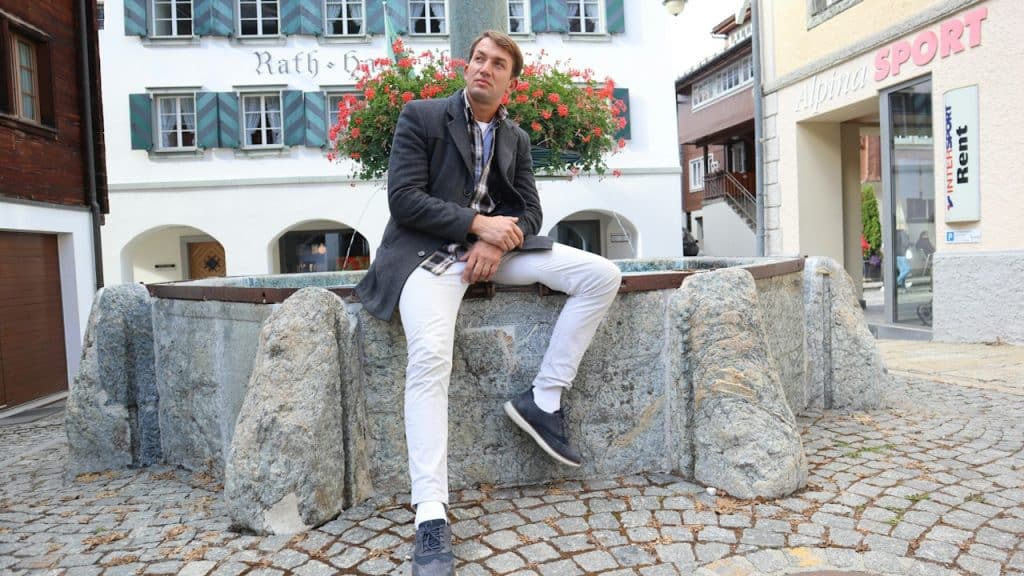 A man sitting on a fountain on a stone-paved street.