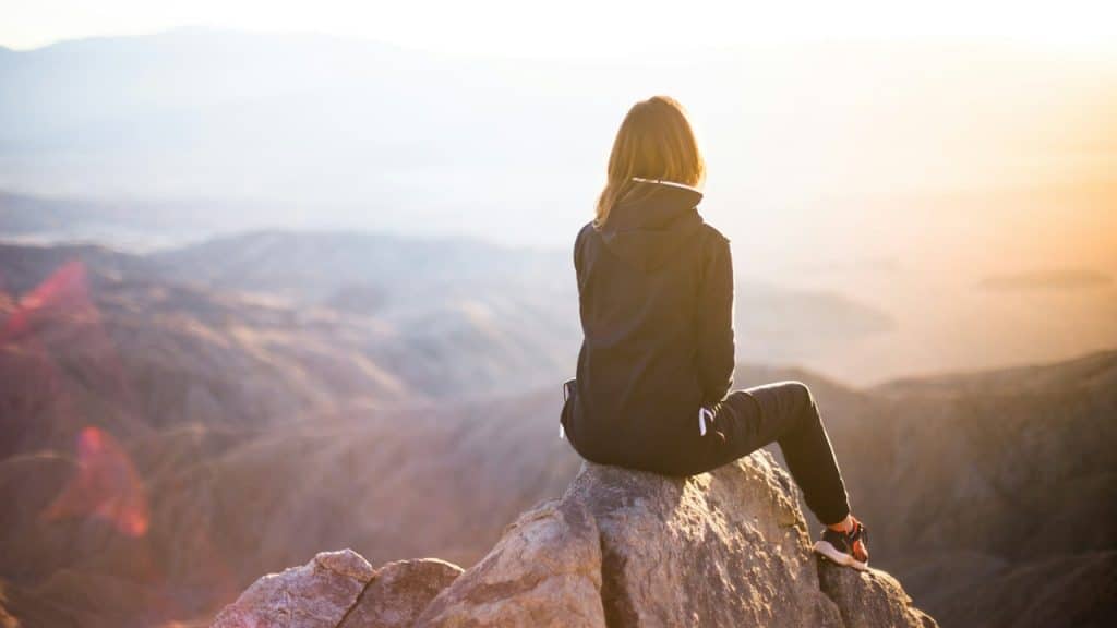A woman is sitting on a rock overlooking a breathtaking view of the mountains.