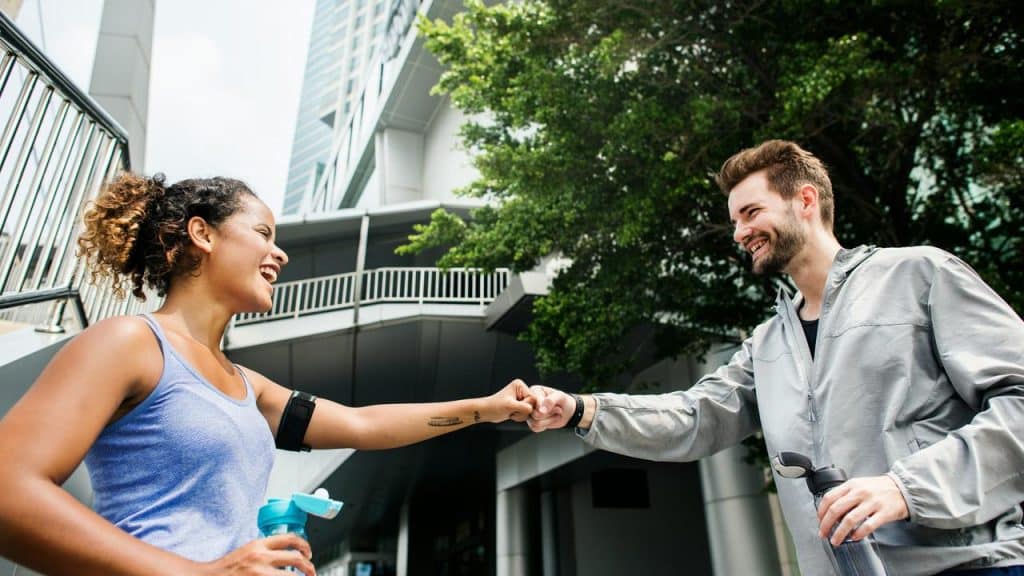 A man and woman smile while bumping fists outdoors.