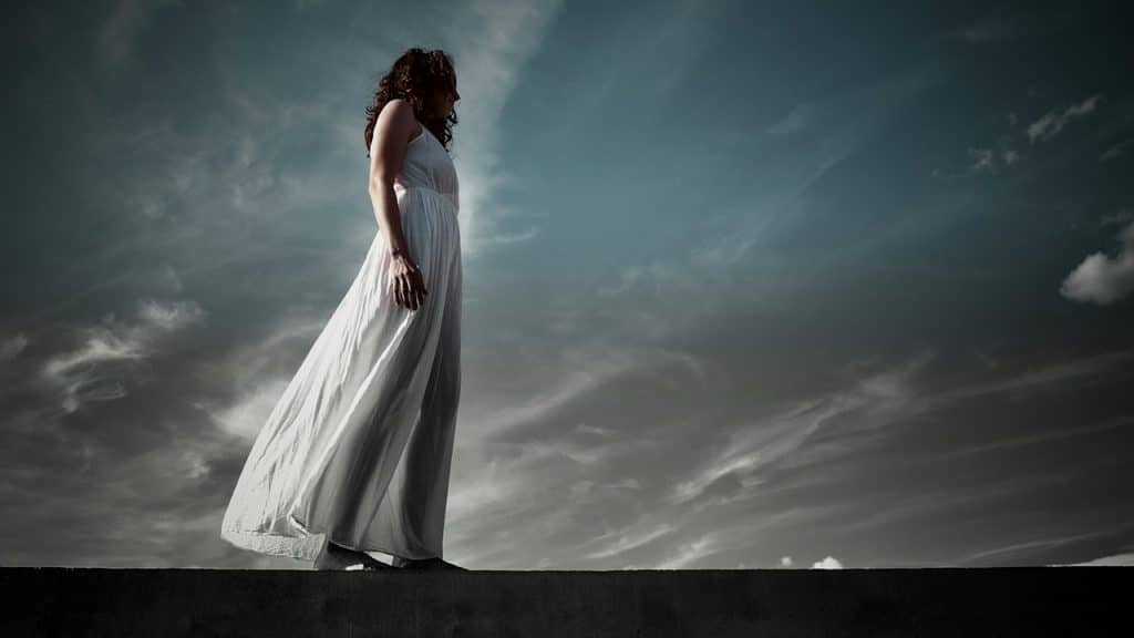 A woman in a white dress standing against a dramatic sky.