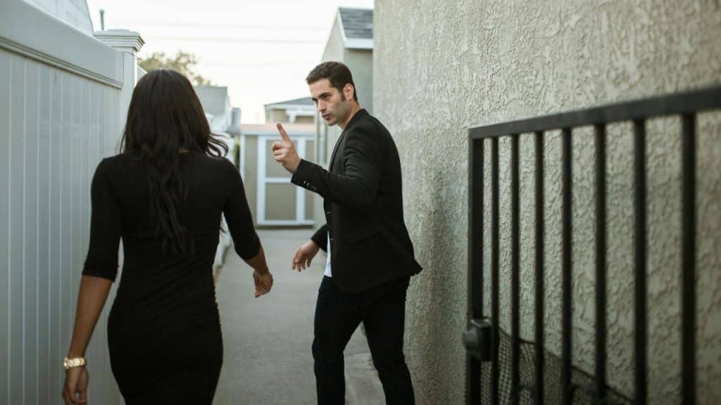 A man points upward and looks back while walking away from a woman outdoors.