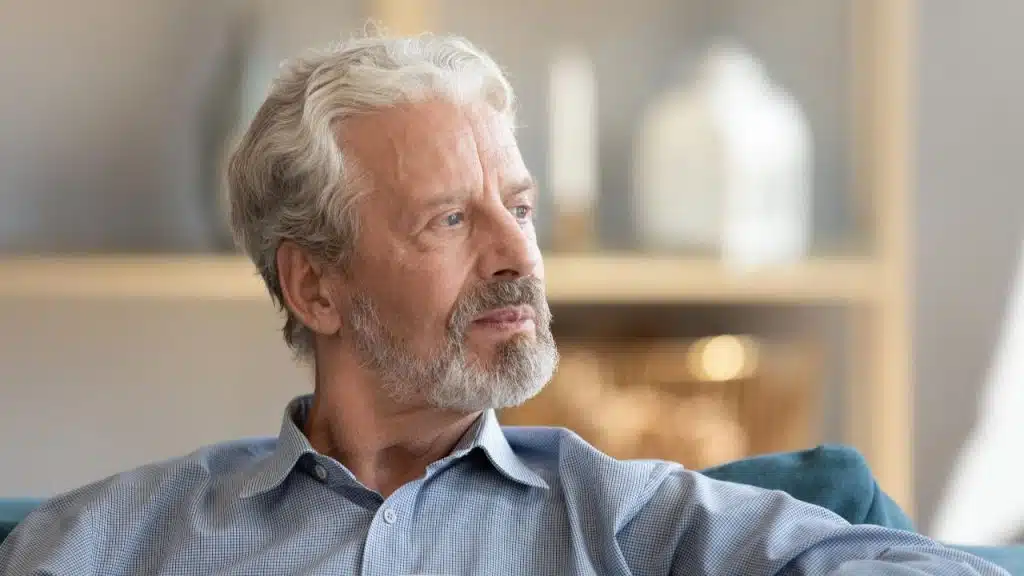 A senior man with wavy gray hair and a beard looking thoughtfully off to the side.