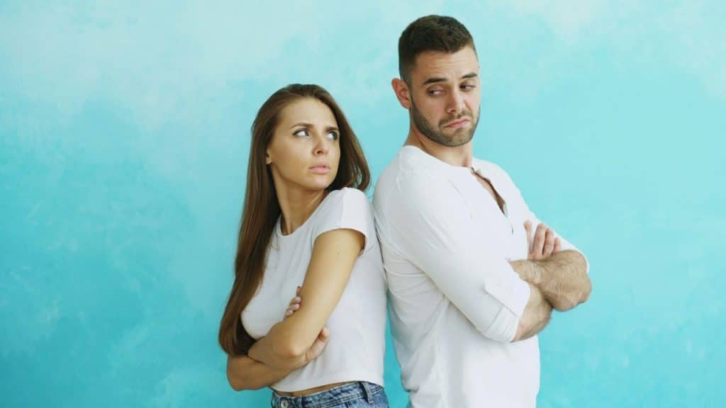 A man and woman stand back-to-back with crossed arms against a bright blue wall.