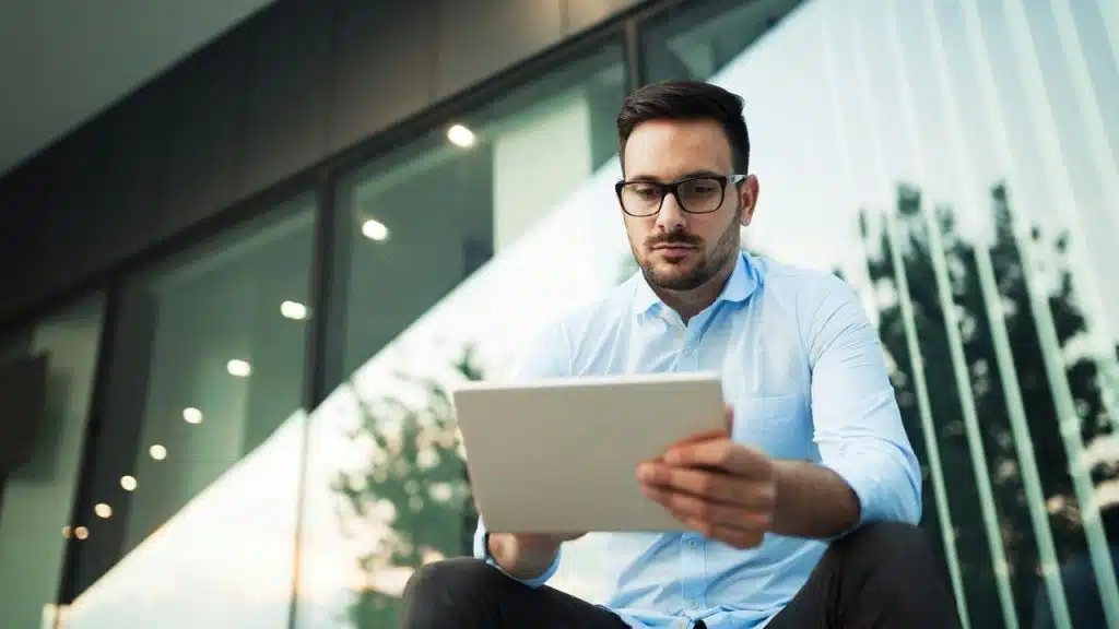 A man in glasses using a tablet outside a building.