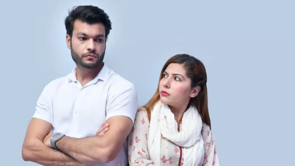 A man and woman stand back-to-back with neutral expressions, looking in opposite directions.