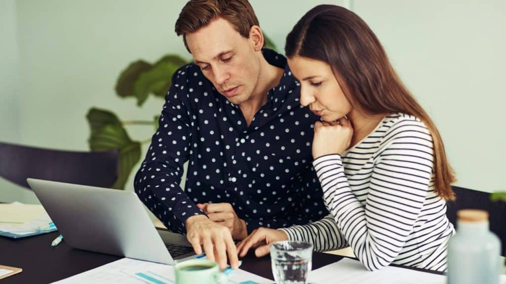 A man points at a laptop screen while a woman sits beside him with her hand on her chin.