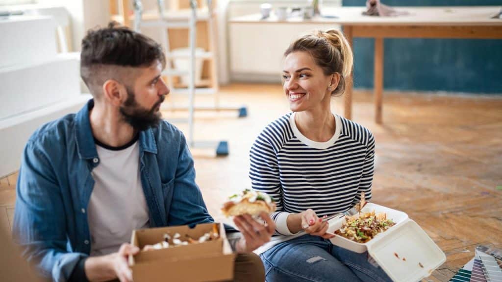 A couple sitting on the floor eating takeout during a home renovation.