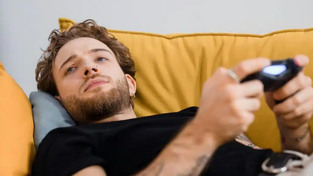 A man lies on a couch holding a video game controller.