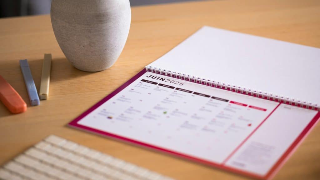 A close-up of a calendar for June 2026 on a wooden desk next to markers.
