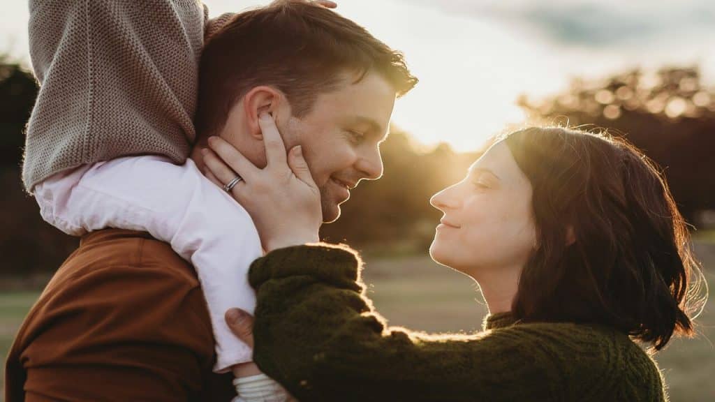 A couple looking at each other while their baby is on the husband’s shoulders