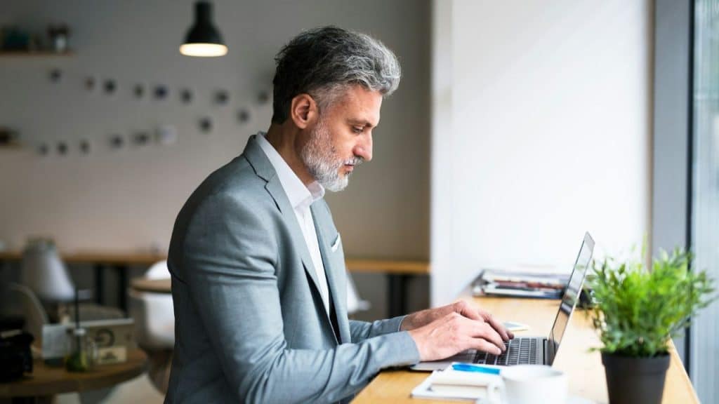 A man with gray hair in a suit types on a laptop at a counter.