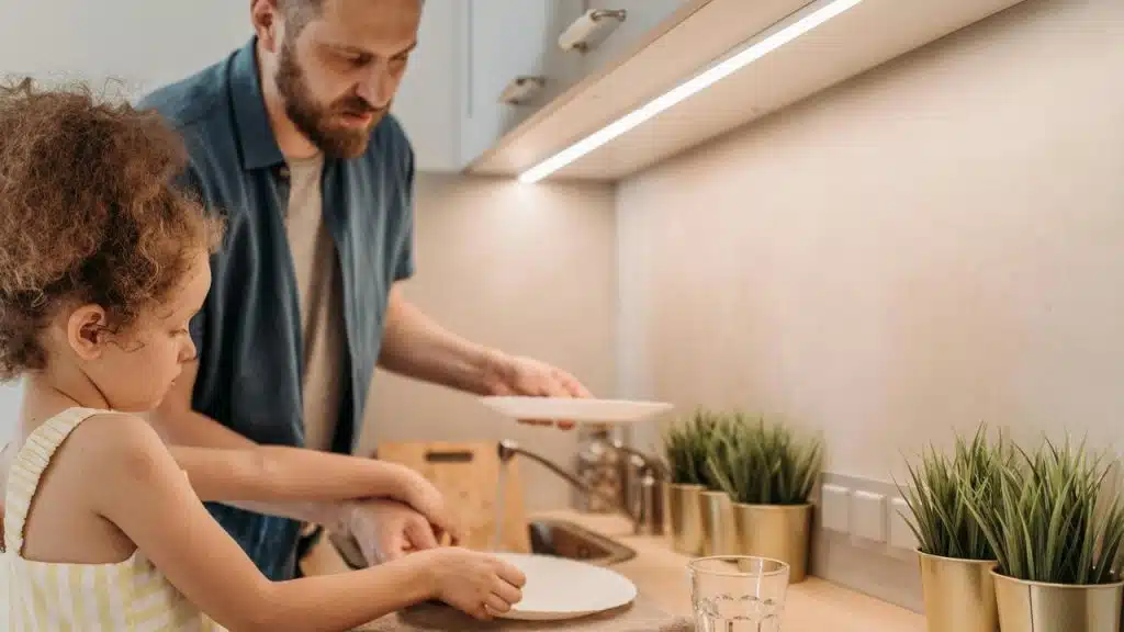 A father and daughter washing dishes together in the kitchen.