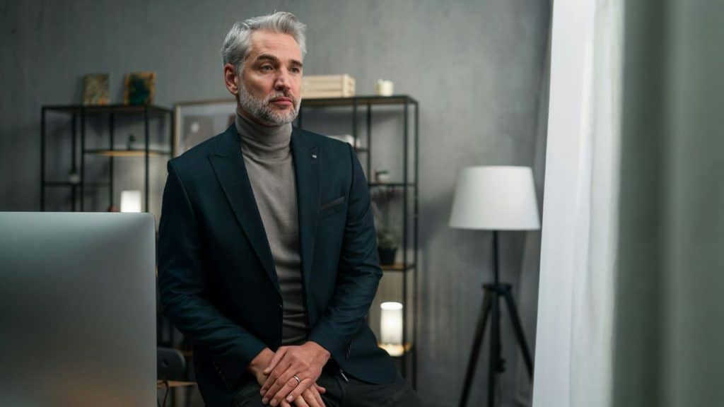 A middle-aged man with grey hair and a beard wearing a dark blazer in an office.