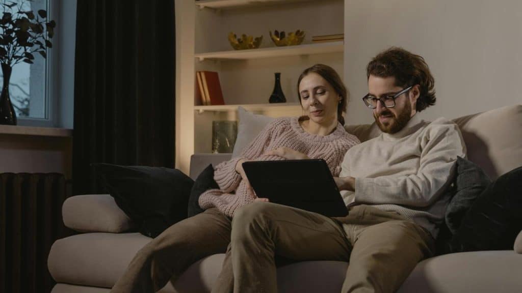 A couple sitting on a couch looking at a tablet together.