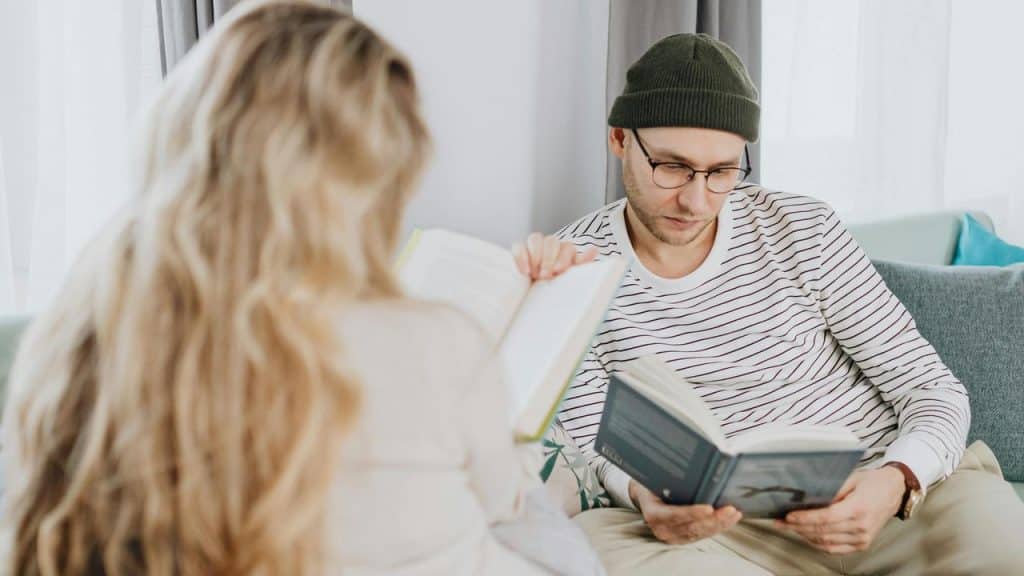 A couple sitting on a couch reading books together.