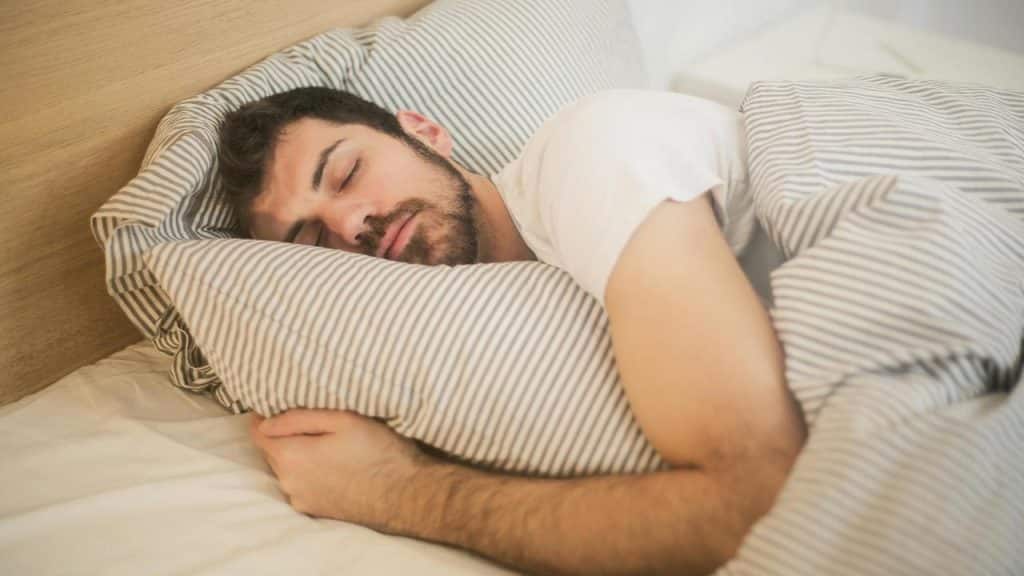 A man sleeping in bed while hugging a striped pillow.