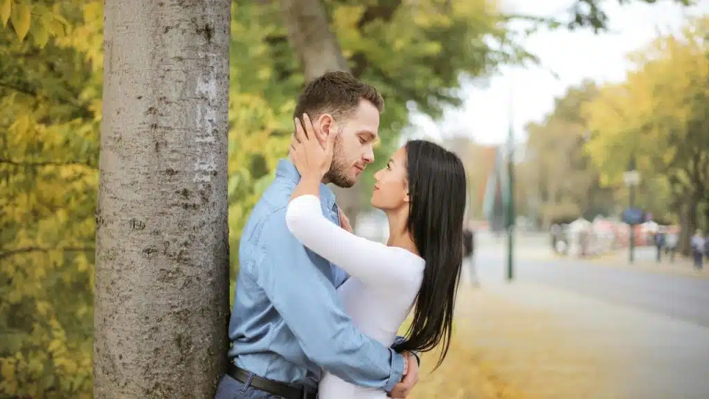 A couple standing close together by a tree