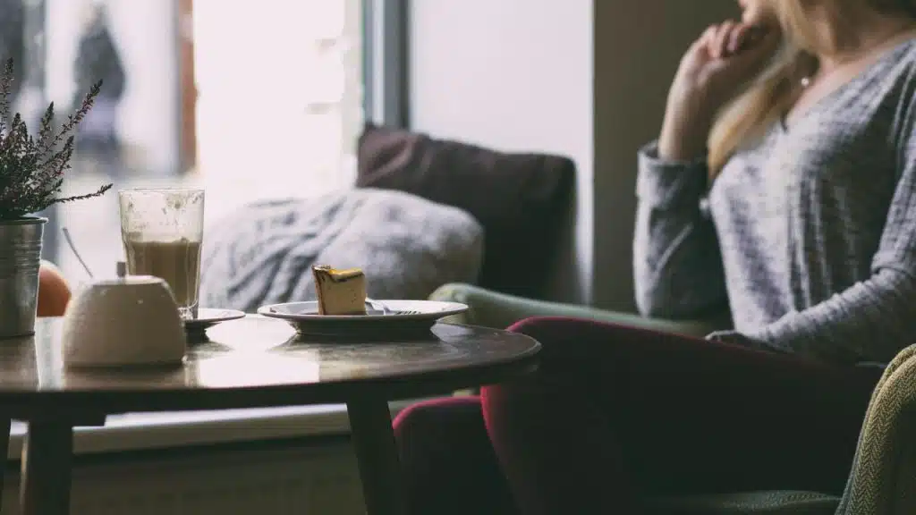 A woman sitting by a table with coffee and cake.