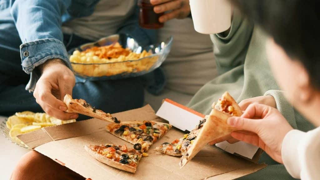 A group of people sharing slices of pizza from a cardboard box.