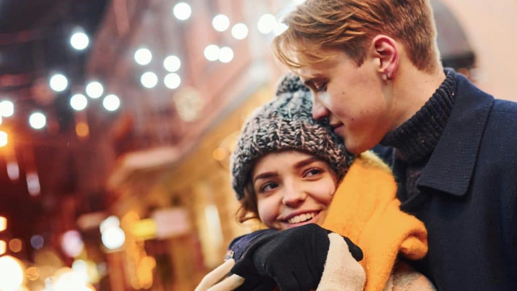 A couple embracing warmly on a city street at night with glowing lights.