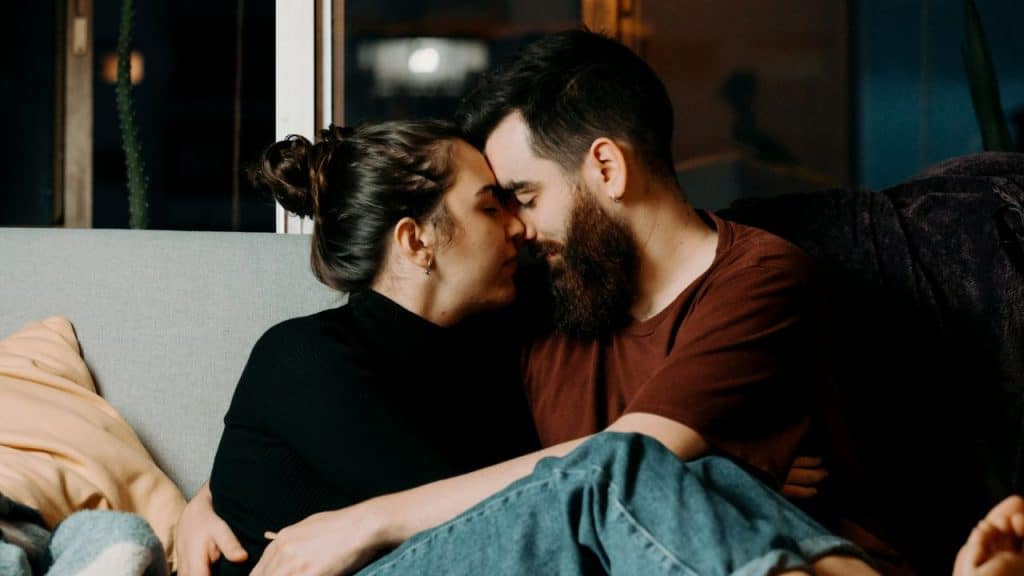 A man and woman touch foreheads while sitting together on a couch at night.