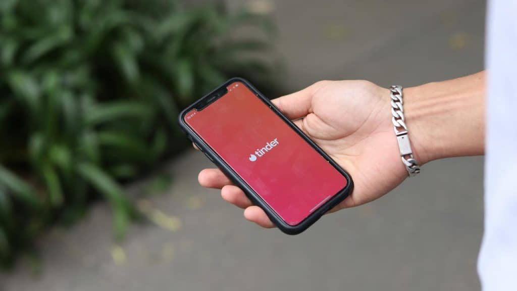 A person holds a smartphone displaying the Tinder app screen.