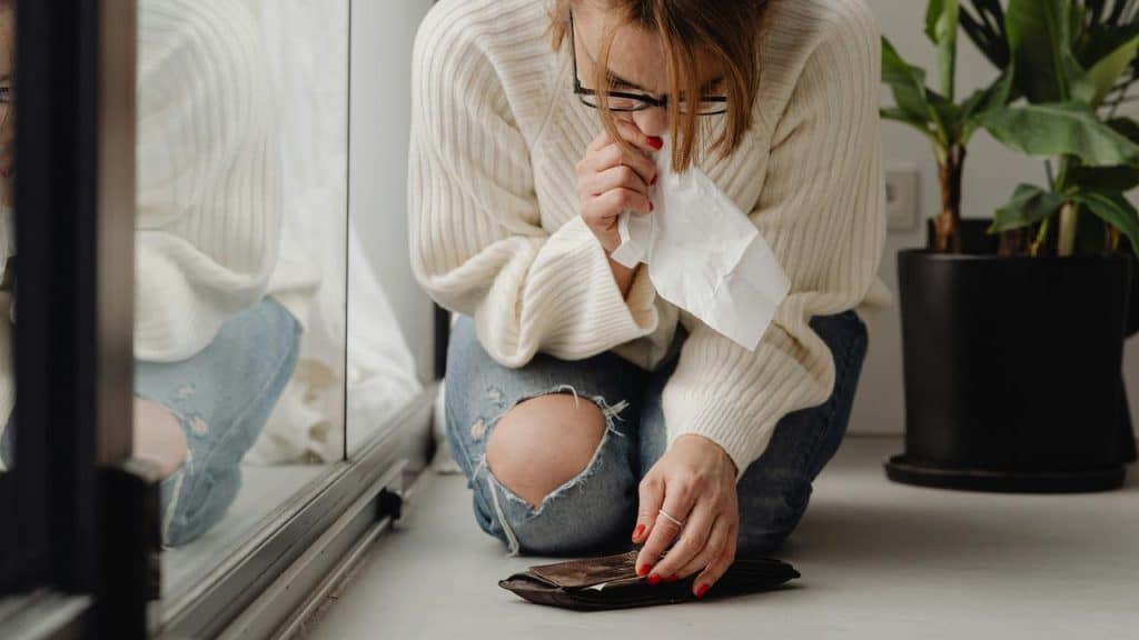 A woman kneeling on the floor crying while holding a tissue and looking at a wallet.