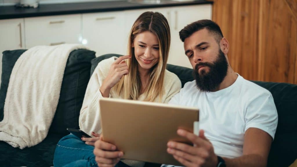 A man and woman sit together on a sofa looking closely at a gold tablet.