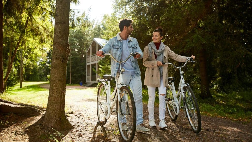 A couple standing with bicycles on a sunny forest path.
