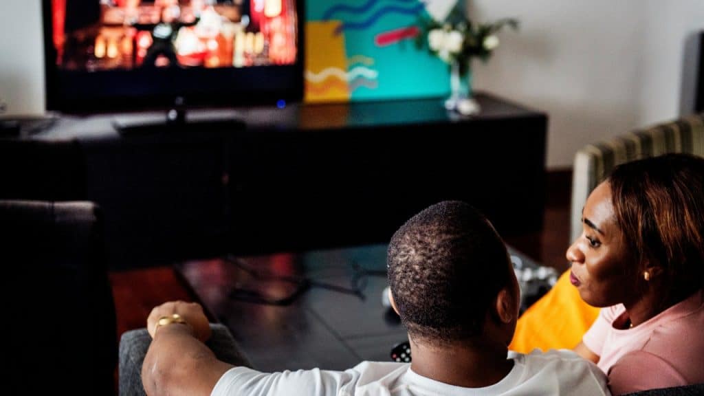 A high-angle view of two people on a couch watching a bright television screen.