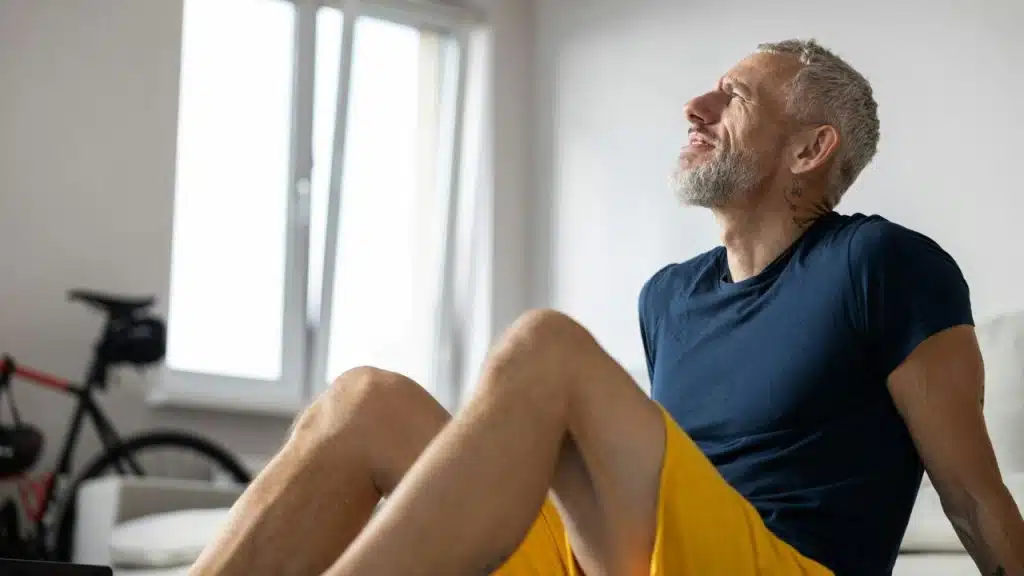 A man with gray hair and a beard sits on the floor looking up.