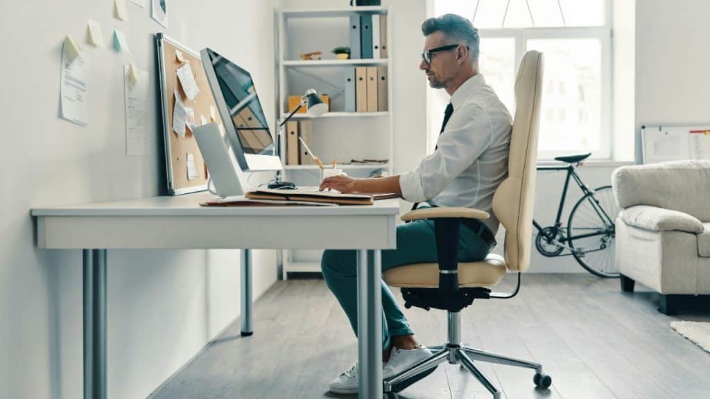 A man in a white shirt and glasses sits at a desk using a large computer.