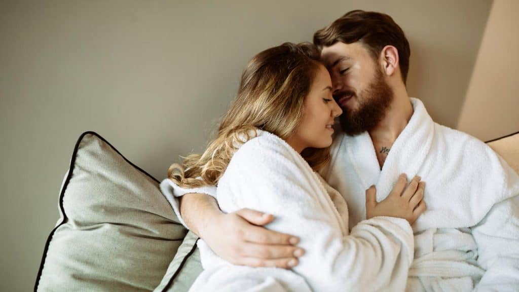 A couple cuddling closely on a couch while wearing white robes.