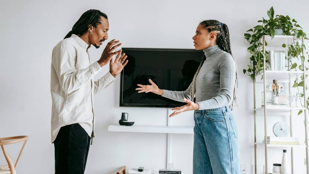 A man and woman stand facing each other with raised hands during an intense discussion.