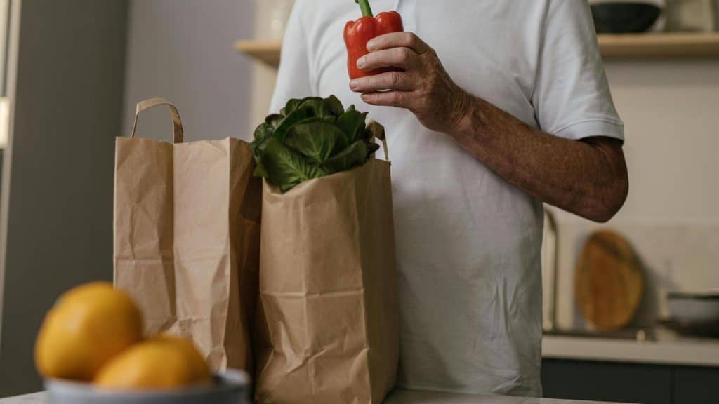 A person holding a red bell pepper near grocery bags on a kitchen counter.