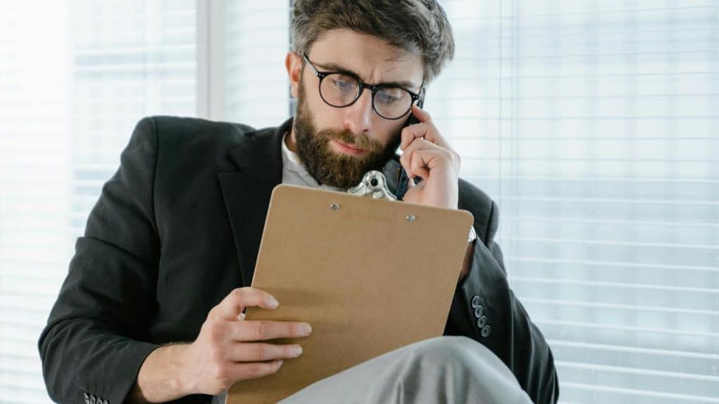 An office worker talking on the phone while reading a clipboard.