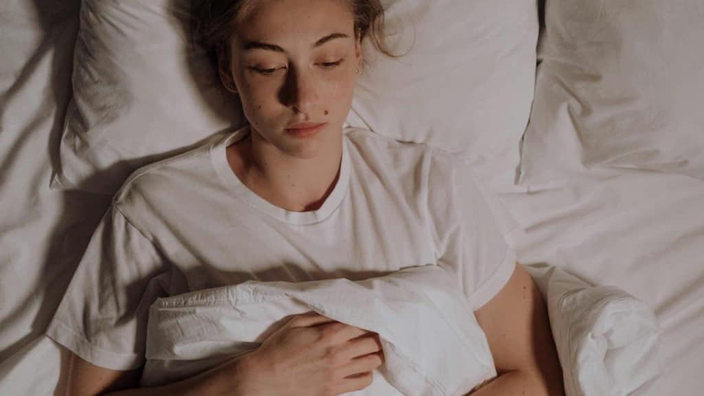 A woman lying in bed, looking down with a thoughtful expression.