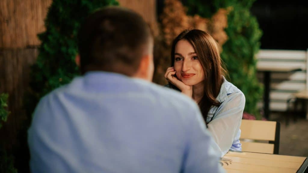 A woman rests her chin on her hand while looking at a man's blurred back.