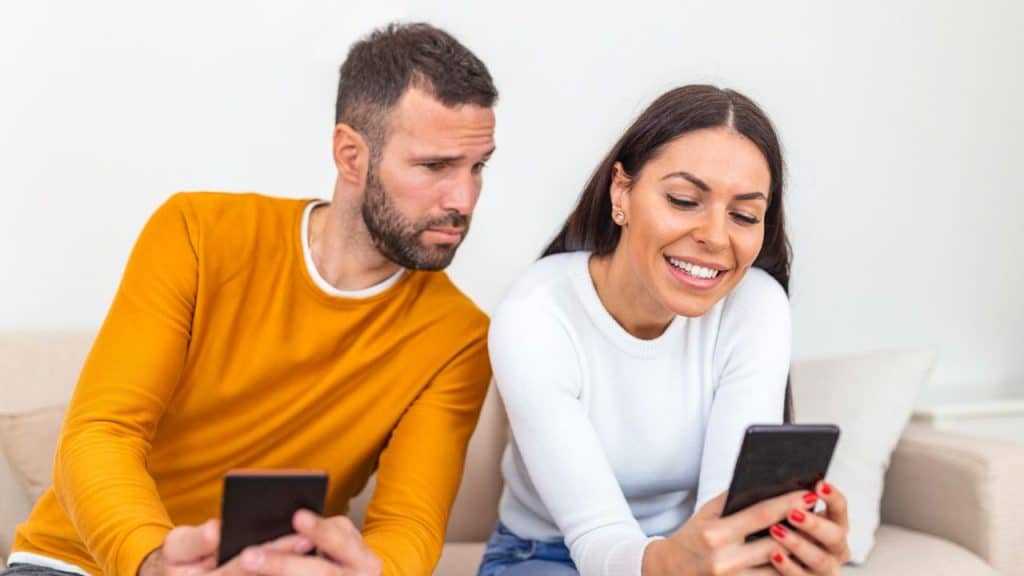 A smiling woman looks at her phone while a man beside her looks at her screen