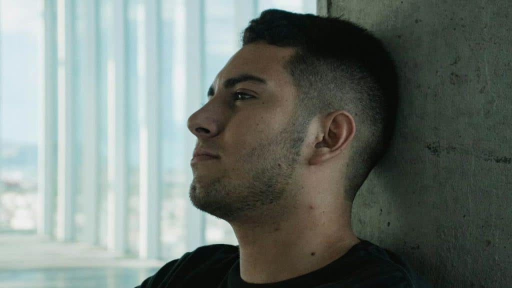 Close-up of a young man with a fade haircut leaning against a concrete wall.