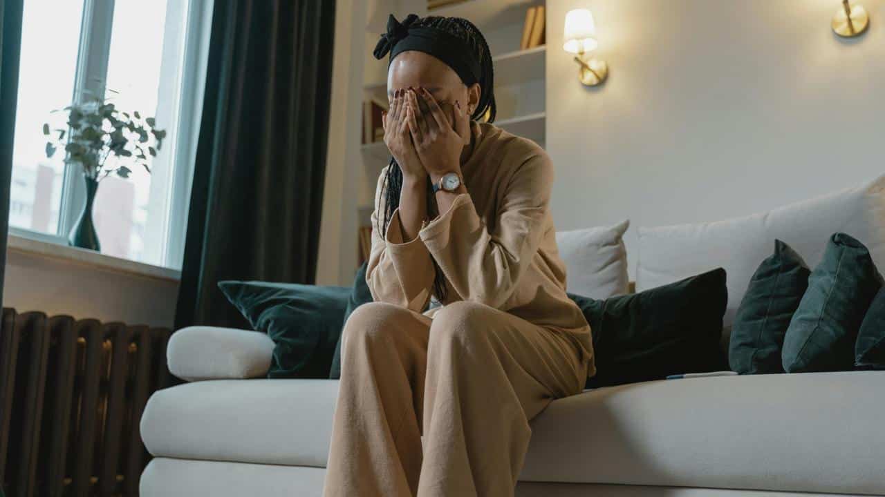 A woman sitting on a couch with her face in her hands, appearing upset.
