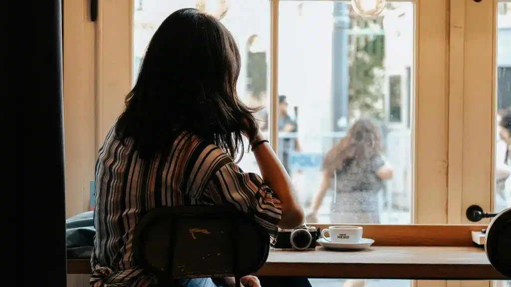 A woman sitting by a window with coffee and a camera.