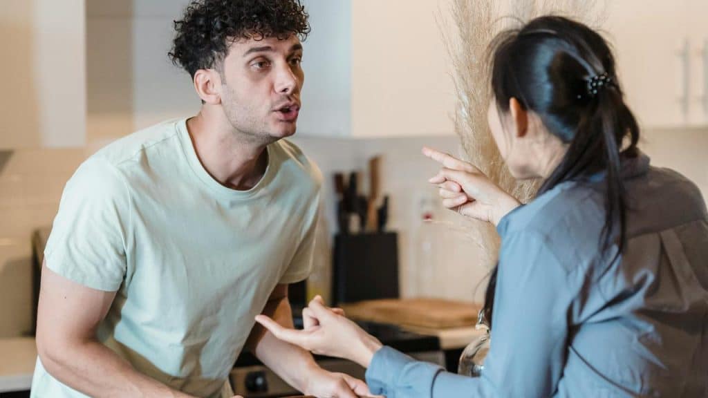 A man and woman arguing in a kitchen with tense expressions.