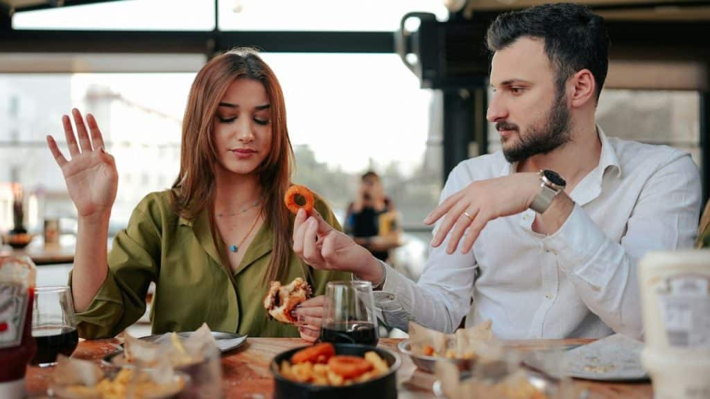 A man holds an onion ring toward a woman while they eat at a restaurant.