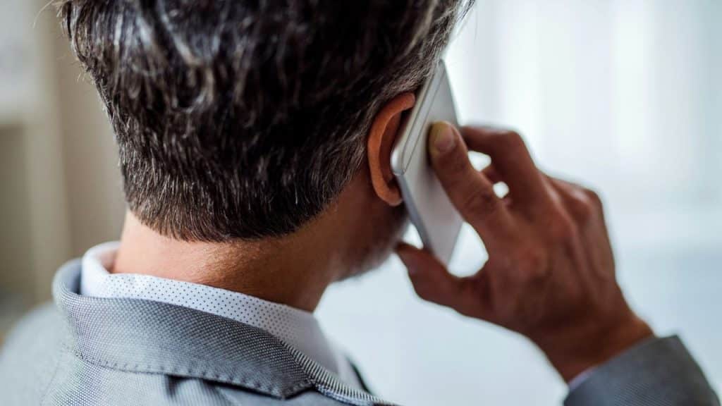 Close-up back view of a person with salt-and-pepper hair holding a phone to their ear.