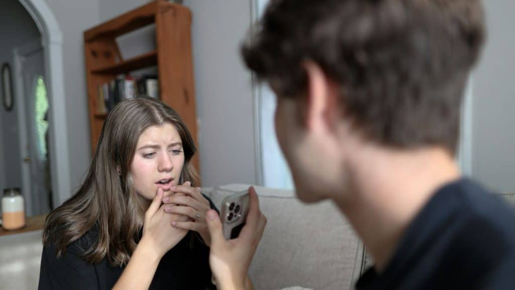 A woman looks concerned while a man in the foreground holds a smartphone toward her.
